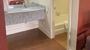 A compact hotel room with a bathroom featuring a sink, mirror, and a telephone. - Travel Inn San Antonio (San Antonio)