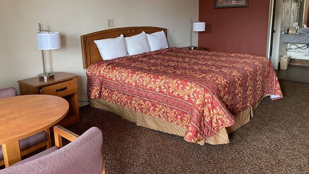 A hotel room with a large bed, a wooden nightstand, a table with chairs, and a painting on the wall. - Travel Inn San Antonio (San Antonio)