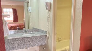 A hotel bathroom with a granite countertop, a white sink, a mirror, a hairdryer, and a shower. - Travel Inn San Antonio (San Antonio)