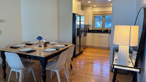 A modern kitchen with white cabinets, a stainless steel refrigerator, and a wooden dining table with chairs. - Spacious 3BR Retreat with Mt. Views, Walk to the lake. 30 days stay! (Whitefish)