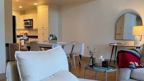 A modern living room with a sofa, a dining table, and a kitchen in the background. - Spacious 3BR Retreat with Mt. Views, Walk to the lake. 30 days stay! (Whitefish)