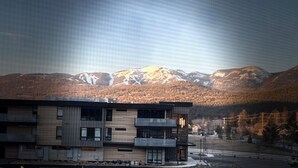 A modern building with multiple floors and balconies, set against a backdrop of snow-capped mountains and a clear sky. - Spacious 3BR Retreat with Mt. Views, Walk to the lake. 30 days stay! (Whitefish)