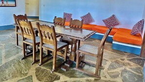 A dining area with a wooden table and chairs, a sofa with patterned cushions, and a wall with a painting. - Silver Rock Hotel (Malindi)