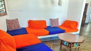A modern living room with a sectional sofa in orange and blue, a small wooden coffee table, and patterned cushions. - Silver Rock Hotel (Malindi)