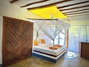 Habitación con una cama bajo un dosel amarillo, un separador de madera y vistas a espacios verdes al exterior.