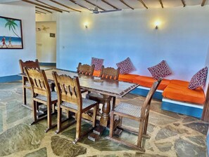 Un comedor con una mesa y sillas de madera, un sofá con cojines estampados y una pared decorada con un cuadro.