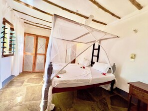 Habitación con cama bajo un dosel, una escalera de madera, una mesita y una puerta con un panel trenzado.
