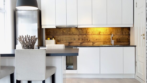 A modern kitchen with white cabinets, a wooden accent wall, a black countertop, and a pendant light.