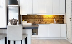 Una cocina moderna con armarios blancos, un muro decorativo de madera, una encimera negra y una lámpara colgante.