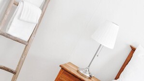 A bedroom with a wooden nightstand, a lamp, a bed with a blue blanket, and a wooden ladder leaning against the wall.