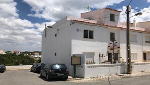 A two-story building with a white facade and red-tiled roof. There are parked cars in front, and a street lamp is visible.
