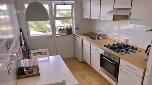 A compact kitchen with white cabinets, a gas stove, a dishwasher, and a window with a view of the outside.