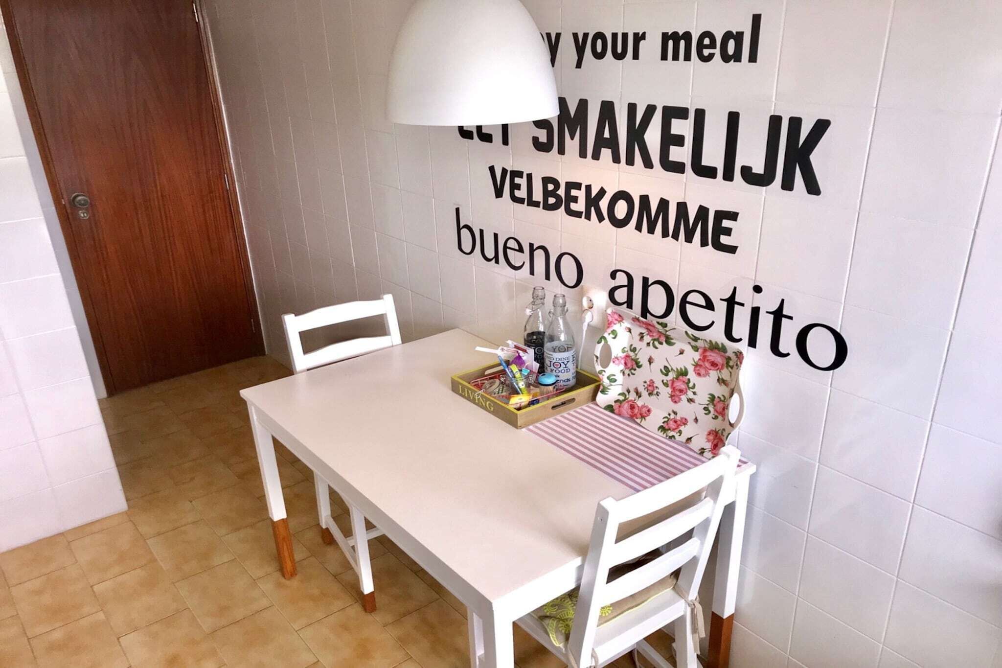 Un espace repas avec une table blanche, des chaises et un mur orné d’un texte inspirant.