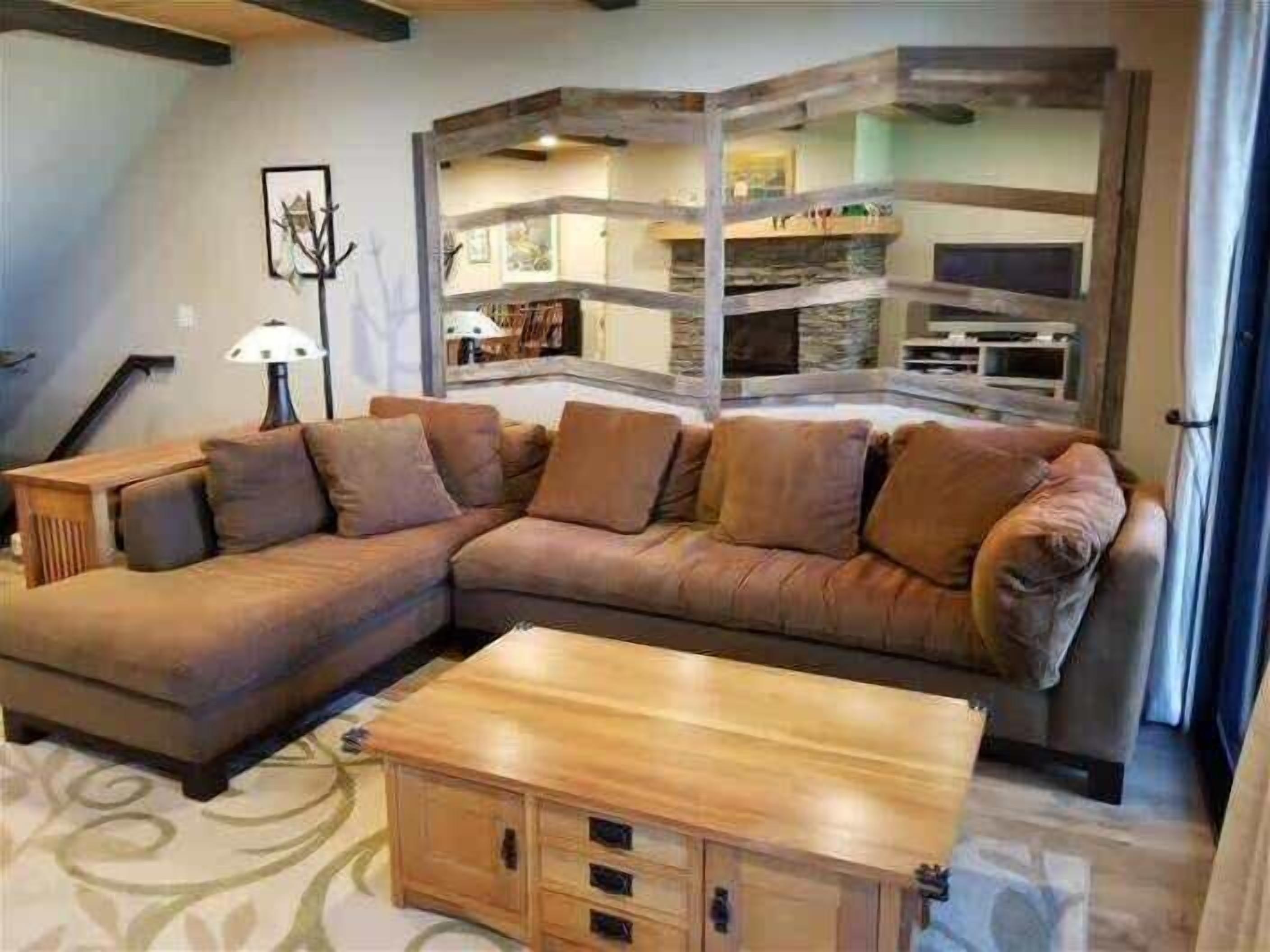 Un salon comprenant un canapé d’angle, une table basse en bois et un escalier menant à un niveau supérieur.