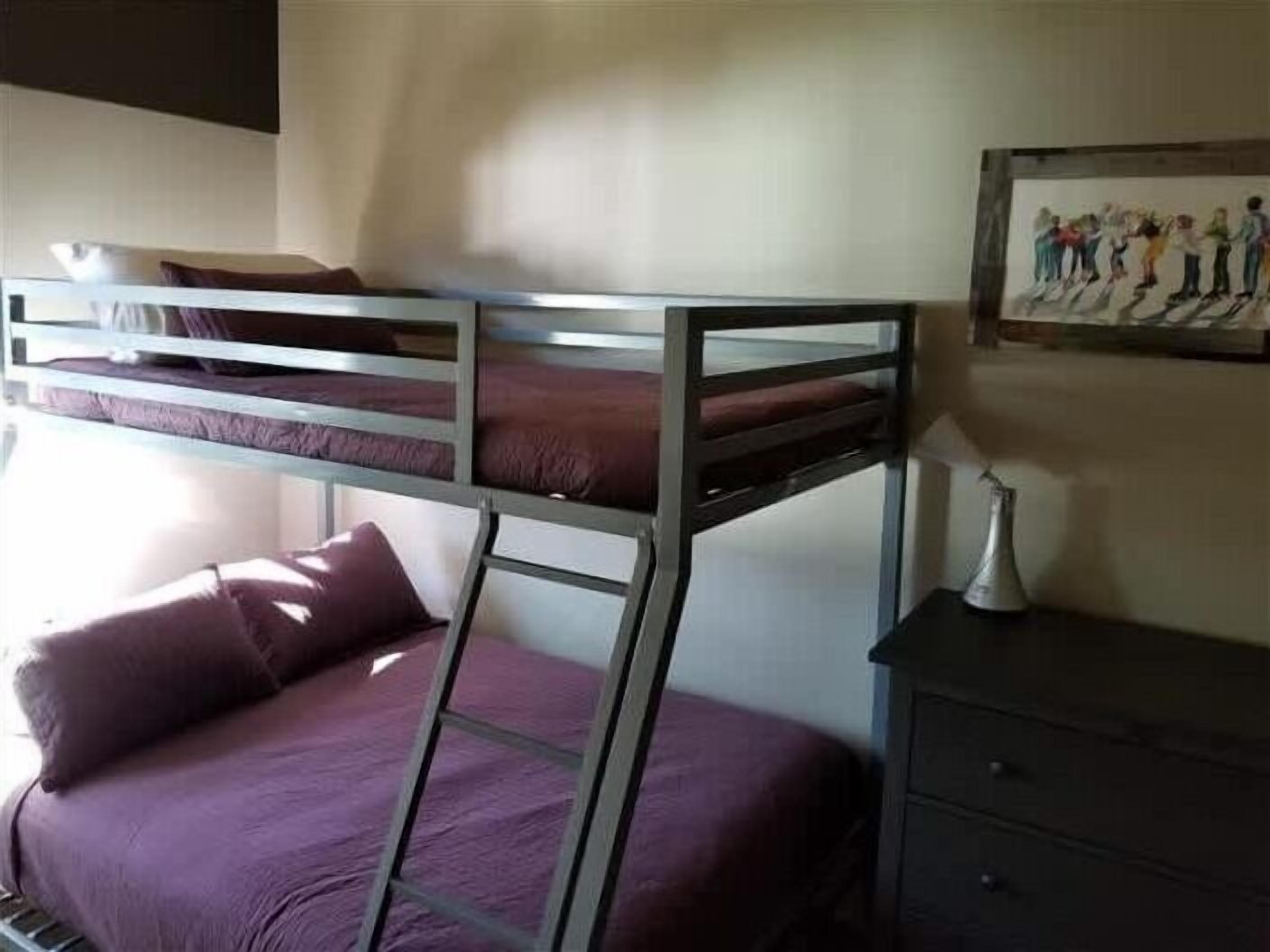 A bunk bed with purple bedding, a small dresser, and a framed artwork on the wall.