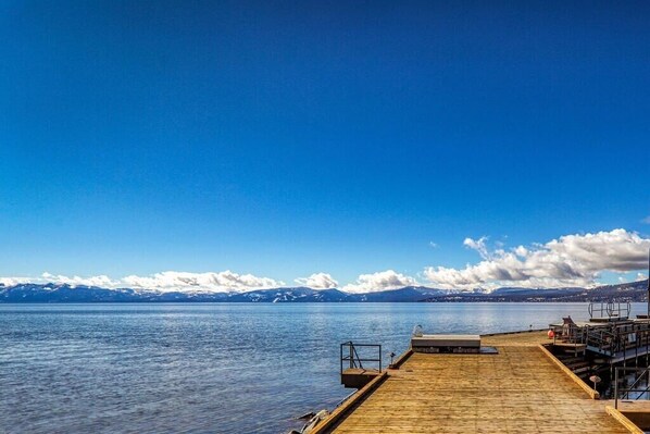 A wooden dock extending into calm water with a clear sky and distant mountains.