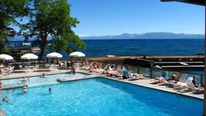 A pool area with lounge chairs and umbrellas, a view of the sea, and a mountainous landscape in the background. - Lakefront Condo in Kings Beach- #19 (Kings Beach)