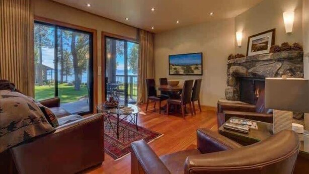 A spacious living room with a fireplace, large windows, and a dining area. - Lakefront Condo in Kings Beach- #19 (Kings Beach)