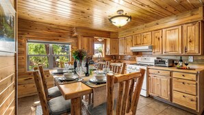 A wooden interior with a dining table set for six, kitchen cabinets, and a large window.