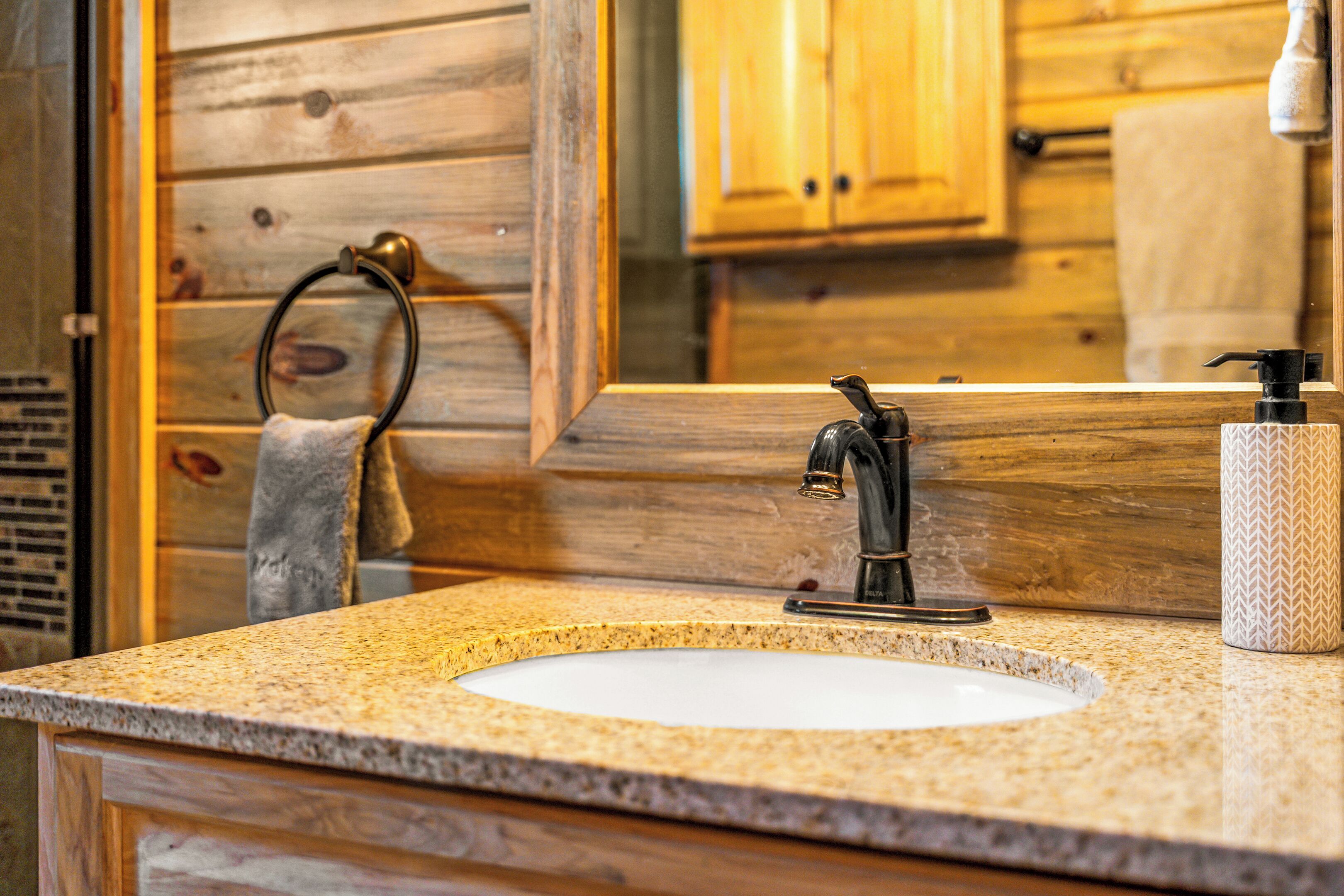 A bathroom with a granite countertop sink, a wooden vanity, a towel ring, and a mirror.