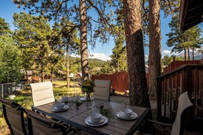 Un área de comedor al aire libre con una mesa dispuesta para dos personas, rodeada de árboles y una valla de madera.