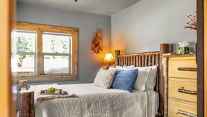 A bedroom with a bed, a dresser, a window, and a wall-mounted lamp.