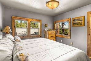 Un dormitorio con cama, cómoda, ventanas y candelabro.