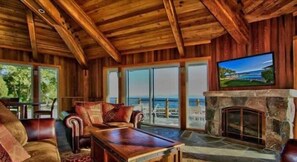 A wooden interior with a stone fireplace, leather furniture, and a large window overlooking a scenic view. - Lakefront Condo in Kings Beach- #25 (Kings Beach)