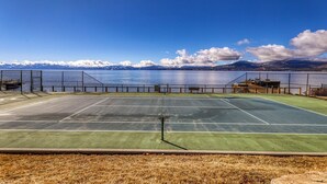 Een tennisbaan met uitzicht op een meer en bergen.