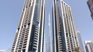 Two high-rise buildings with a central spire, surrounded by palm trees and other modern structures.