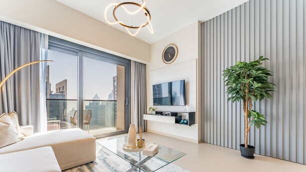 A modern living room with a glass coffee table, a sofa, a TV, and a potted plant.