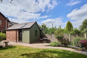 A small, green shed with a sloped roof and a door, adjacent to a brick building.
