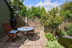 A patio with a round table and two wooden chairs, a wooden fence, and a small pond.