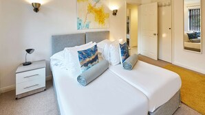 Un dormitorio moderno con una cama grande, una mesita de noche, una lámpara y una obra de arte colgada en la pared.