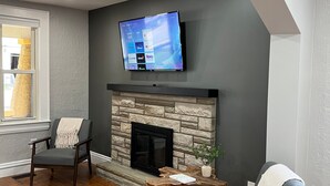 Ein Wohnzimmer mit einem Kamin aus Stein, einem darüber montierten Flachbildfernseher und zwei Sesseln.
