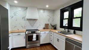 Eine moderne Küche mit weißen Schränken, einem Edelstahlbackofen, einem Geschirrspüler und einer Marmor-Spritzschutzwand.