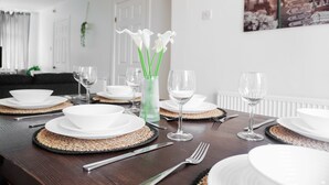 Een eettafel gedekt met witte borden, kommen en bestek, met een vaas witte bloemen.