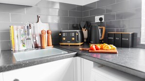 Een keuken met een modern design, met een zwarte broodrooster, een koffiezetapparaat en een snijplank met fruit.