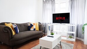 Een moderne woonkamer met een grijze bank, een witte salontafel en een tv waarop 'NETFLIX' wordt weergegeven.