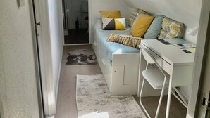 A compact, well-lit room with a bed, a desk, and a small rug.