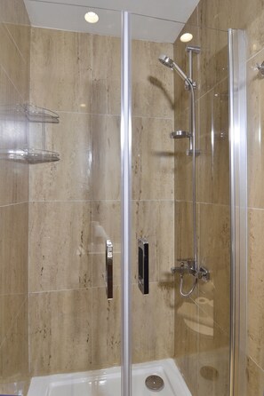 Eine begehbare Dusche mit Glaswand, einer Handbrause und einem am Wand montierten Wasserhahn.