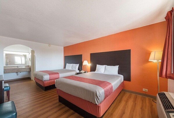 Habitación de hotel con dos camas, un escritorio, una silla, un espejo y una lámpara.