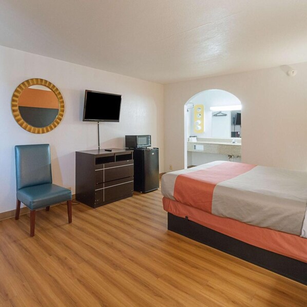 Un dormitorio con cama, un escritorio con televisor, una silla y un espejo.