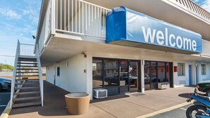 A building with a 'welcome' sign, a covered entrance, a staircase, and a parked motorcycle. - Motel6 San Antonio, TX - I-10 West (San Antonio)