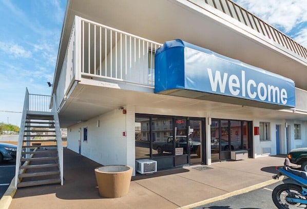 A building with a 'welcome' sign, a covered entrance, a staircase, and a parked motorcycle.