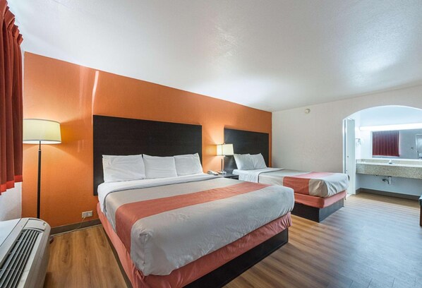 A hotel room with two beds, a desk, a lamp, and a bathroom visible through an archway. - Motel6 San Antonio, TX - I-10 West (San Antonio)