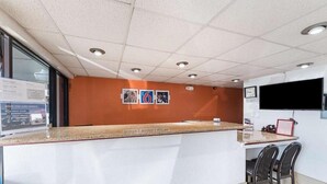 A reception area with a counter, a TV mounted on the wall, and a bulletin board with pictures. - Motel6 San Antonio, TX - I-10 West (San Antonio)