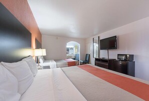 Habitación de hotel con una cama grande, un escritorio con silla, televisor, microondas y una pequeña kitchenette.