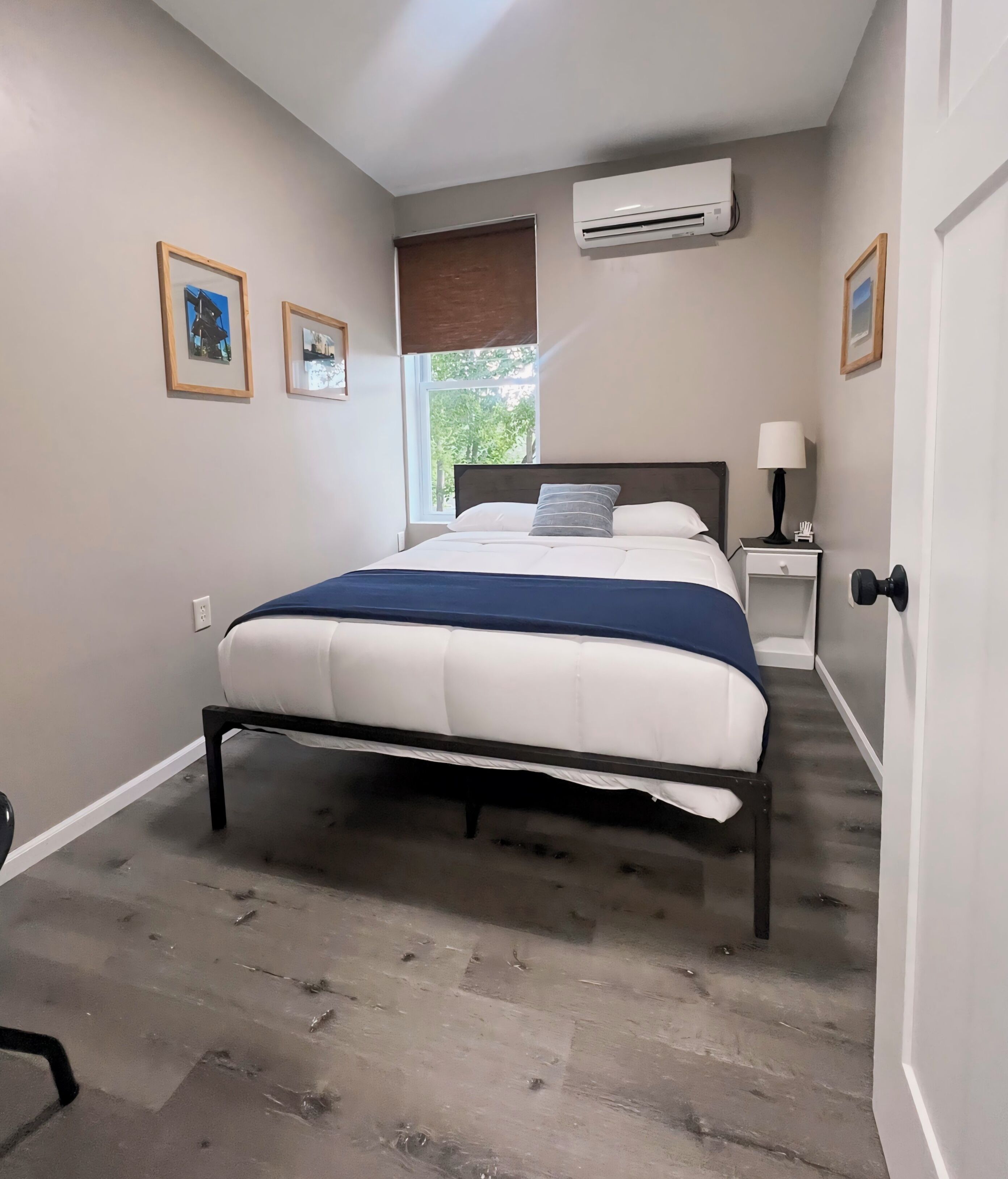 Ein Schlafzimmer mit Bett, Fenster mit Blick, Klimaanlage und gerahmten Bildern an der Wand.
