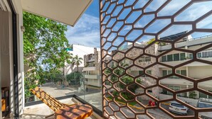 A balcony with a wooden table and chairs, a metal fence, and a view of a street with buildings and parked cars. - Ocean View Apt 2 blocks away from beach (Playa del Carmen)